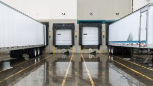 Trucking Industry and Logistic Dock  - two trailers are parked at the dock with two empty spots int between them reminding us to look for how to find shippers as a freight broker
