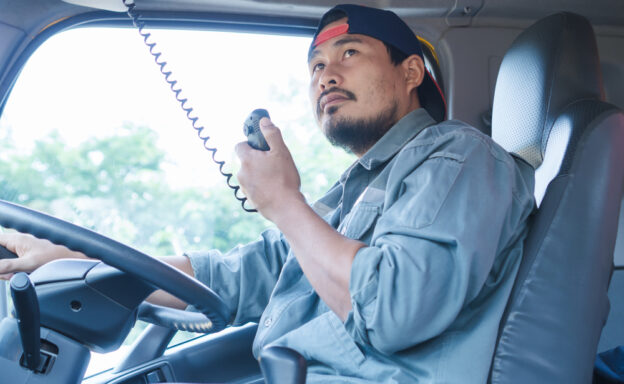 An Asian male truck driver using his radio to communicate - using trucker lingo, trucker slang