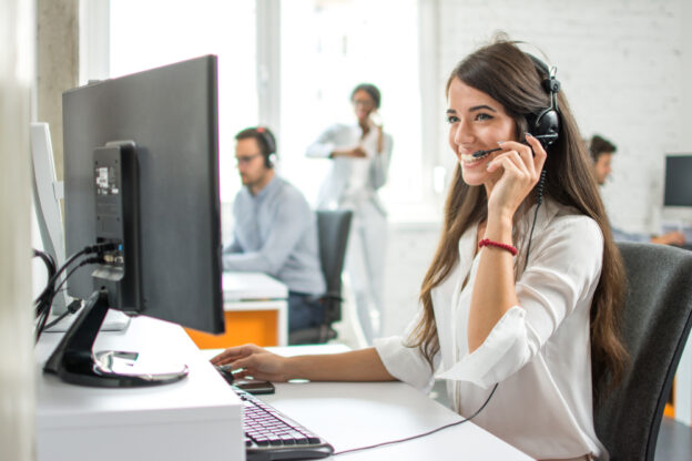 female freight broker, sitting at a desk with a laptop, using a headset to call out to freight clients