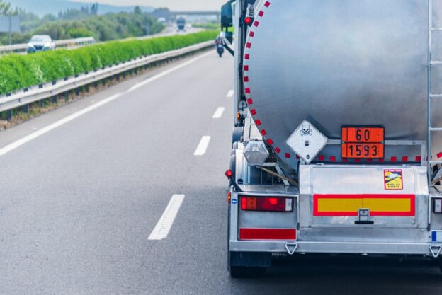 Rear view of a hazardous materials tanker truck, featuring the orange panel with hazard identification number and UN number, and a toxic liquid label.
