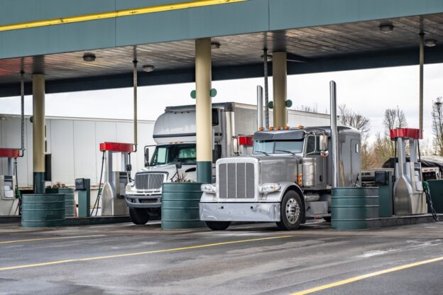 Industrial different class carriers big rig semi trucks with semi trailers fill up their fuel tanks at truck stop gas station for continue route according to the schedule of the electronic log book